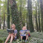 Dwoje dzieci, chłopiec i dziewczynka, czytają książkę w lesie.