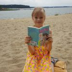 Dziewczynka czyta książkę na plaży. Jest ładna pogoda.