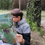 Chłopiec czyta książkę w lesie.
