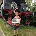 Chłopiec trzyma książkę. W tle lokomotywa.