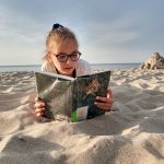 Dziewczynka czyta książkę na plaży.