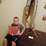 Chłopiec trzyma otwartą książkę na tle eksponatu muzealnego.