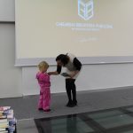 Na scenie kobieta wręcza dziewczynce nagrodę książkową.