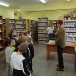 Pomieszczenie biblioteki: grupa dzieci jest witana przez bibliotekarkę