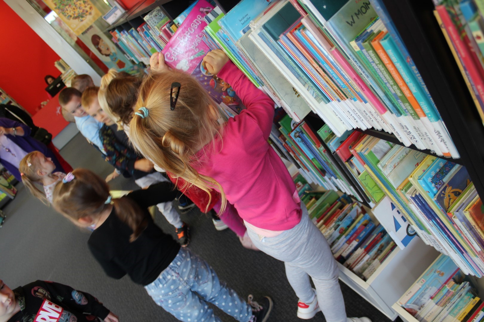 Grupa dzieci stoi przy półce z książkami, ogląda wybrane książki