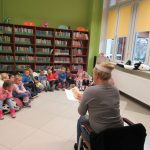 Pomieszczenie biblioteki: Dzieci zasłuchane w bajkę czytaną przez bibliotekarkę