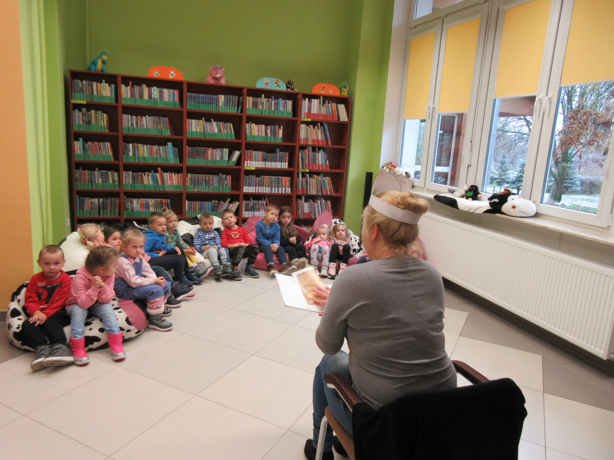 Pomieszczenie biblioteki: Dzieci zasłuchane w bajkę czytaną przez bibliotekarkę