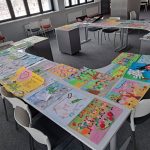 W pomieszczeniu biblioteki na stolikach są rozłożone prace plastyczne dzieci.