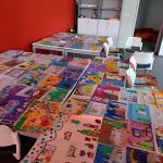 W pomieszczeniu biblioteki na stolikach są rozłożone prace plastyczne dzieci.