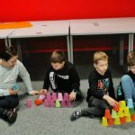 Klub Młodego Programisty. Dzieci siedzą na podłodze. Tworzą wieże w kolorowych kubków