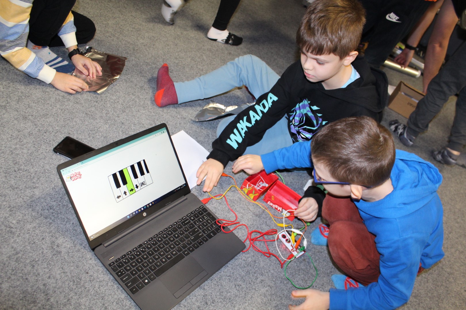 Zajęcia Klubu Młodego Programisty . Dzieci siedzą przy laptopie, do którego podłączony jest zestaw do programowania