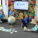 W pomieszczeniu Wypożyczalni dla dzieci, dzieci siedzą w okręgu i patrzą na Panią , która pokazuje na globusie, jak ważna jest wooda. Na drugim planie telewizor, na którym wyświetlone jest logo PAH