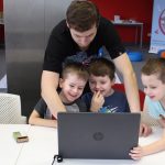 W pomieszczeniu biblioteki ojciec jednego z chłopców pokazuje trójce chłopców funkcje w laptopie