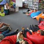 Pomieszczenie wypożyczalni dla dzieci w okręgu siedzą dzieci, które patrzą na bibliotekarkę