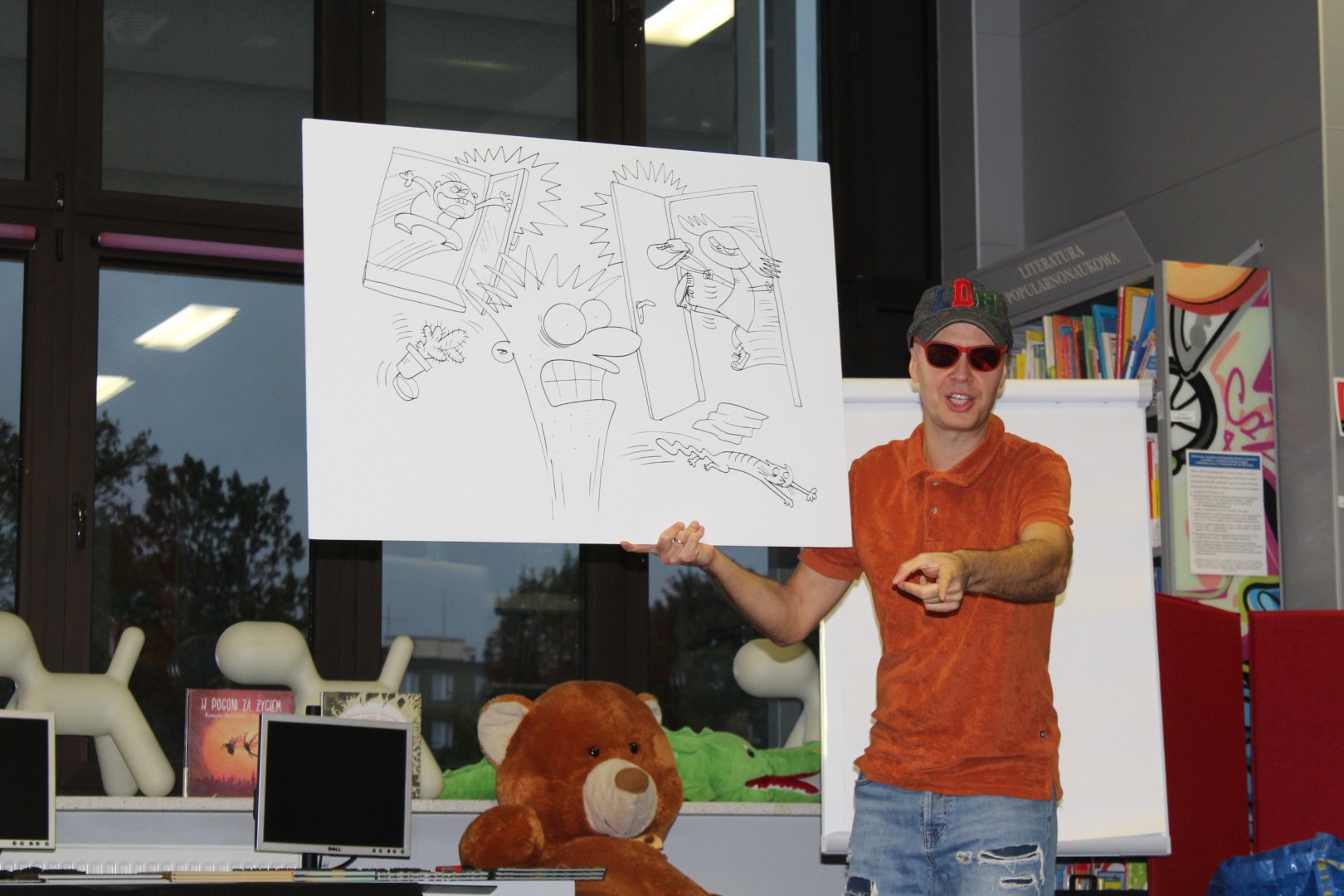 Autor Przemysław Wechterowicz z w czasie spotkania w bibliotece pokazuje uczestnikom planszę z rysunkami