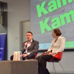 Spotkanie autorskie z Kamilem Kamińskim. Na scenie przy stoliki siedzi autor z prowadzącą spotkanie, na drugim planie ekran z zielonym napisem