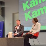 Spotkanie autorskie z Kamilem Kamińskim. Na scenie przy stoliki siedzi autor z prowadzącą spotkanie, na drugim planie ekran z zielonym napisem