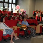 Publiczność w sali widowiskowej siedzi na czerwonych fotelach