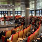 Na scenie przemawiający mężczyzna Franciszek Piątkowski Publiczność podczas spotkania siedzą na czerwonych fotelach patrzą na scenę