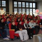 publiczność podczas spotkania siedzą na czerwonych fotelach patrzą na scene