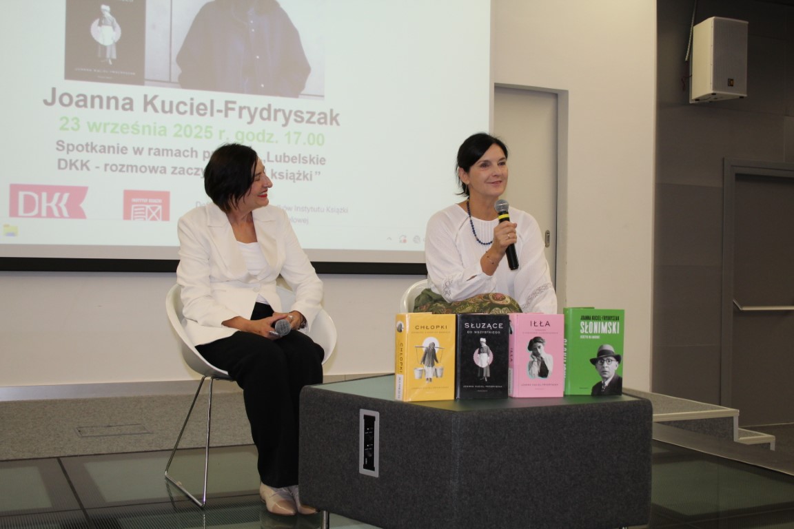 Na scenie sali widowiskowej siedzi autorka Joanna Kuciel Frydryszak, obok prowadząca spotkanie