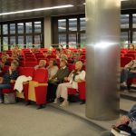 Uczestnicy spotkania siedzą w sali widowiskowej na czerwonych fotelach