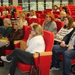 Uczestnicy spotkania siedzą w sali widowiskowej na czerwonych fotelach