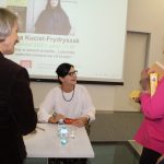 Uczestnicy spotkania wraz z pisarką pozują do zdjęcia. W tle ekran z plakatem