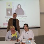 Uczestnicy spotkania wraz z pisarką pozują do zdjęcia. W tle ekran z plakatem