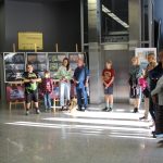 W galerii stoi grupa ludzi, którzy patrzą na autora wystawy. Dookoła prace na sztalugach