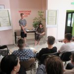 Uczestnicy Narodowego Czytania siedzą i patrzą na ucznia, który recytuje