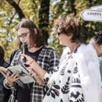 W słoneczny dzień kobieta trzyma mikrofon do którego czyta młody mężczyzna
