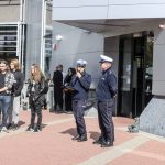 Dwoje policjantów przemawia do tłumu przed budynkiem biblioteki w słoneczny dzień