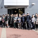Duża grupa młodzieży oraz dorosłych, dwoje policjantów stoi przed budynkiem biblioteki i pozują do zdjęć