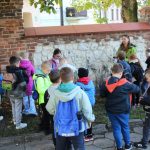 Dzieci stoją przy murze i słuchają kobiety