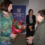 Dwie kobiety patrzą na siebie, jedna daje kwiaty drugiej