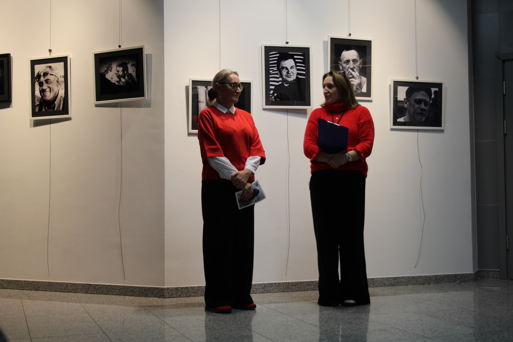 Dwie kobiety ubrane w czerwień stoją w galerii Nova w tle obrazy