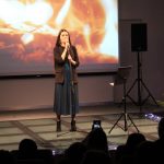 Kobieta stoi na scenie w tle choinka i ekran z płomieniami