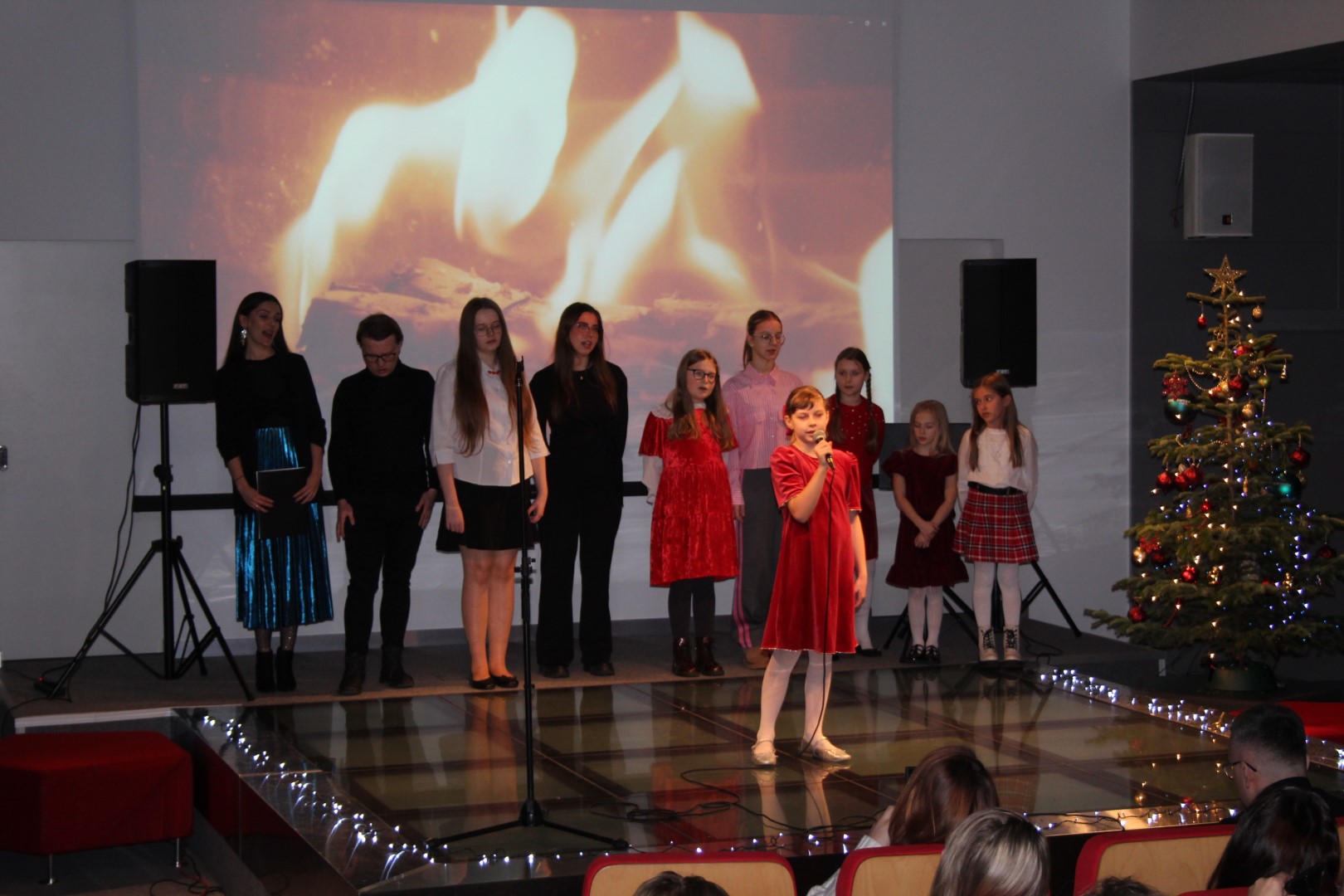 Dzieci stoją na scenie i śpiewają w tle ekran z płomieniami