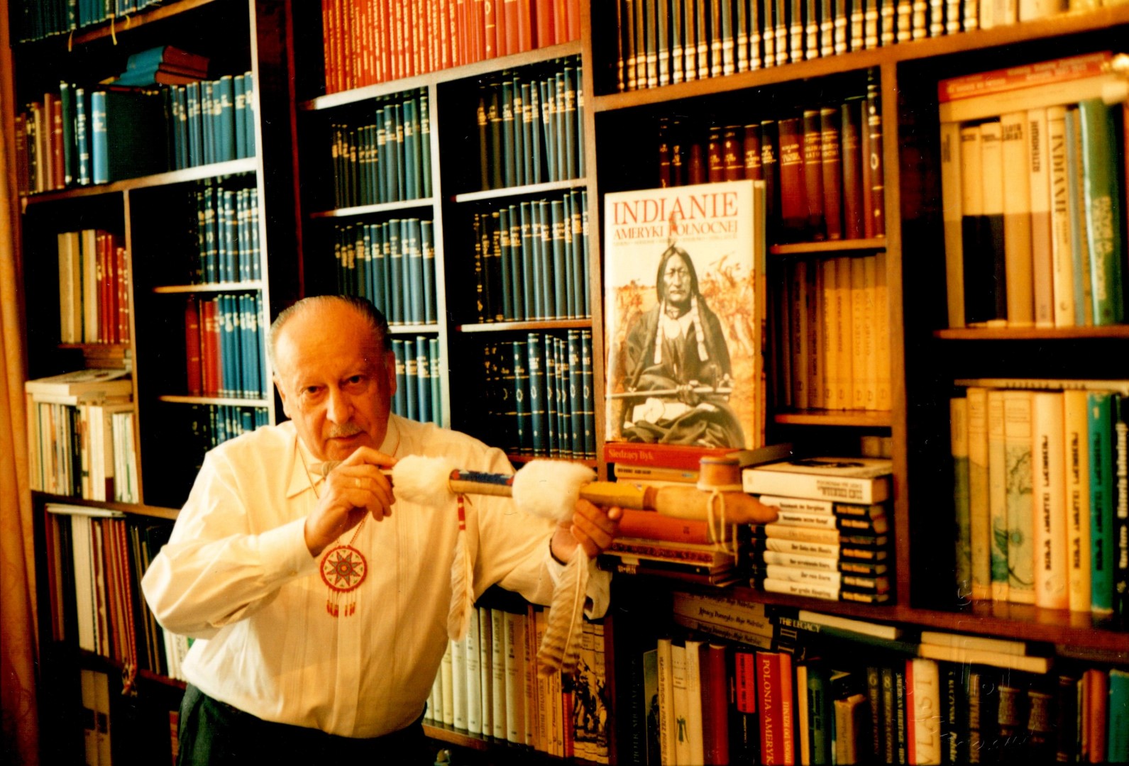 Mężczyzna trzyma kalumet opierając się o regał z książkami