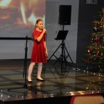 Dziewczynka stoi na scenie w tle choinka i ekran z płomieniami