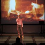 Dziewczynka stoi na scenie w tle choinka i ekran z płomieniami