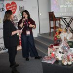 Prowadzące WOŚP stoją obok sceny sali widowiskowej biblioteki