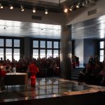 Wojciech Hetman wraz z prowadzącymi na scenie sali widowiskowej biblioteki w tle widzowie spotkania