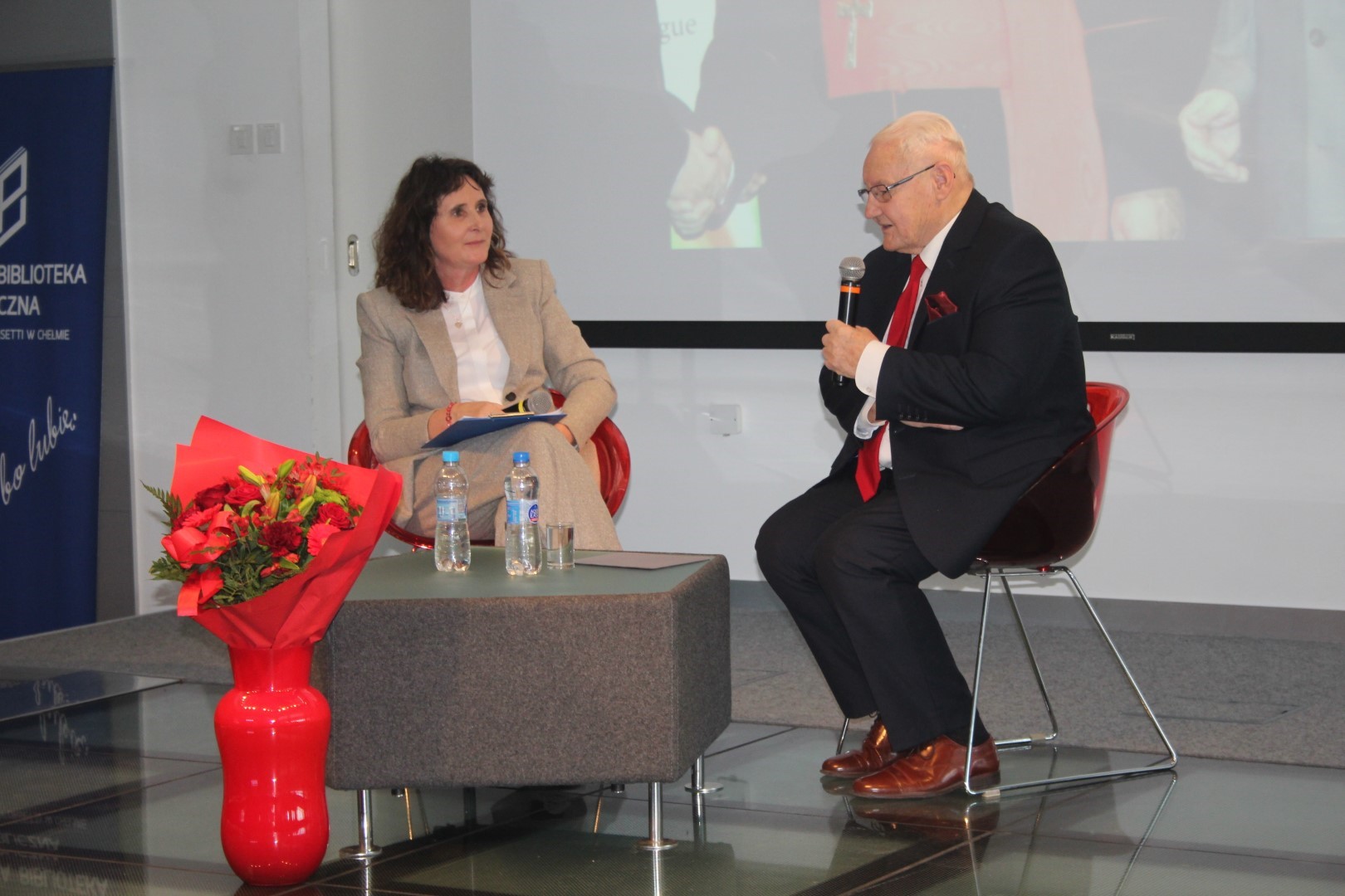 Wojciech Hetman wraz z prowadzącymi na scenie sali widowiskowej biblioteki