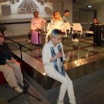 Grupa osób na scenie sali widowiskowej czytają poezję